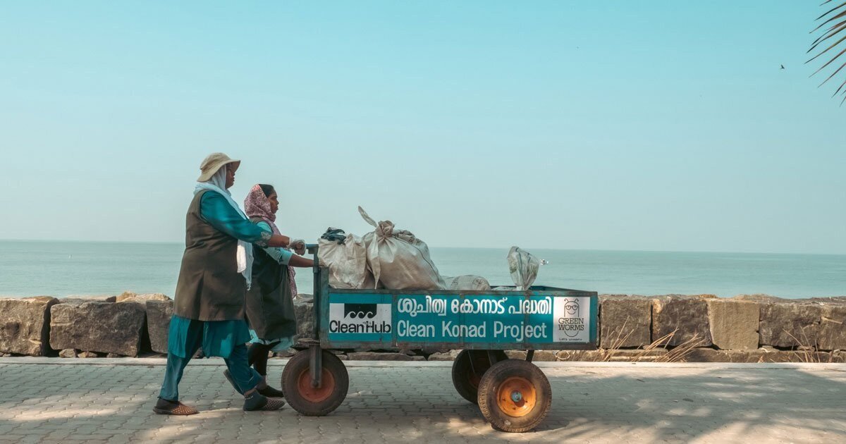 Two collectors push a CleanHub collection cart of sorted plastic along a seawall
