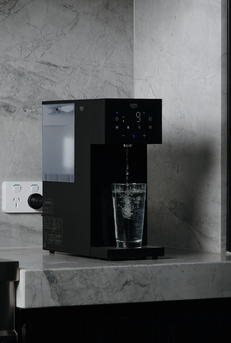 Rippl Nano in Black pouring a glass of water in a marble kitchen
