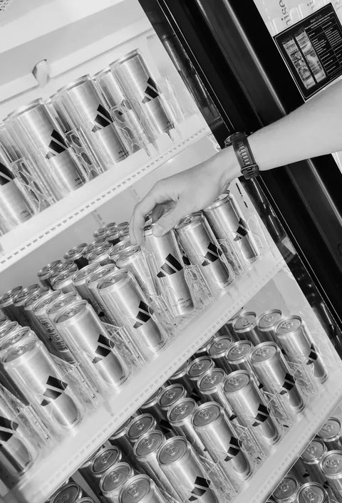 A hand taking an adidas can from a fridge full of them