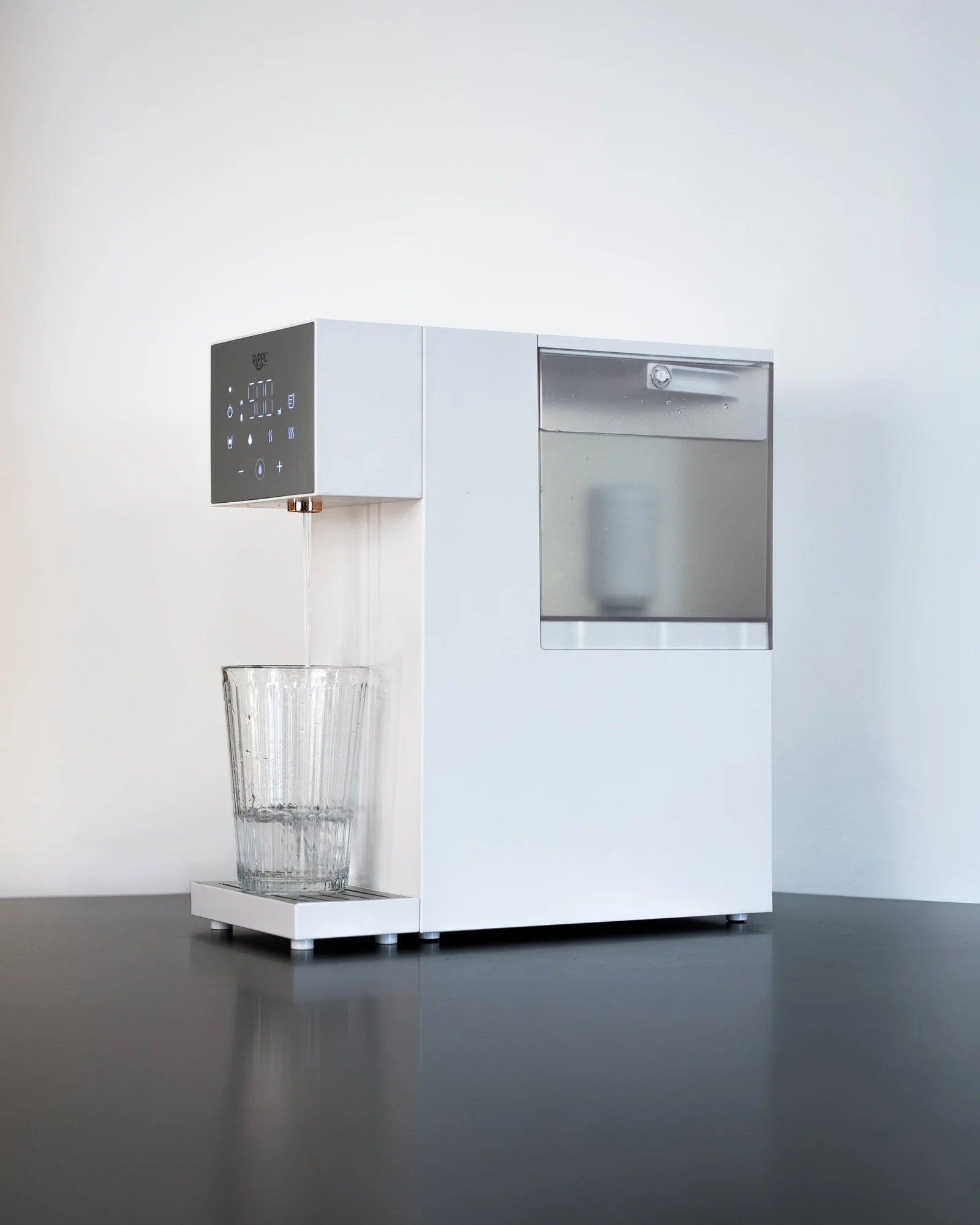 Rippl Nano in White, three-quarter view, the tank and filter visible, a glass of water at the spout